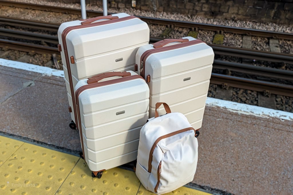 3 cream suitcases with brown trim and a small backpack on a train station platform