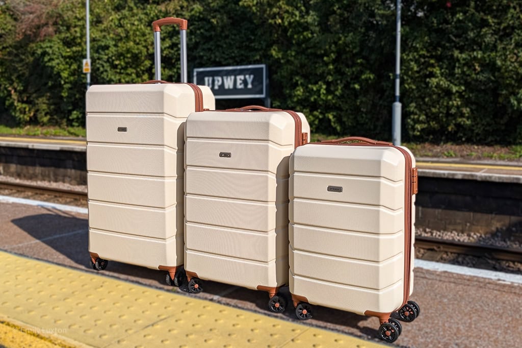 3 cream suitcases with brown trim on a train station platform