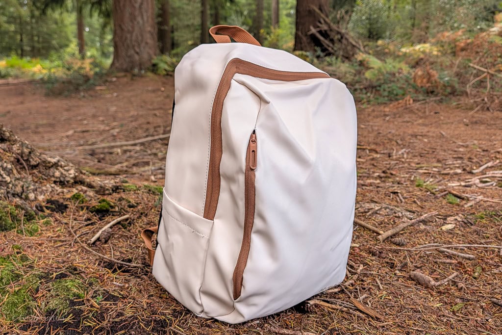 Cream backpack with brown zips and handle on the floor of a woodland