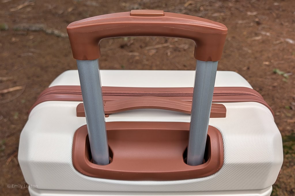 Close up of a brown telescopic handle extended on a cream and brown suitcase