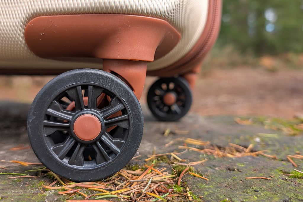 Close up of a black wheel on a cream and brown suitcase