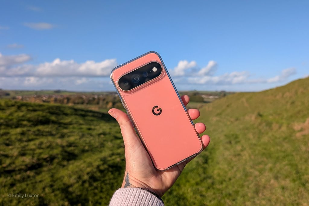 Hand holding a coral Google Pixel phone in front of a grassy field