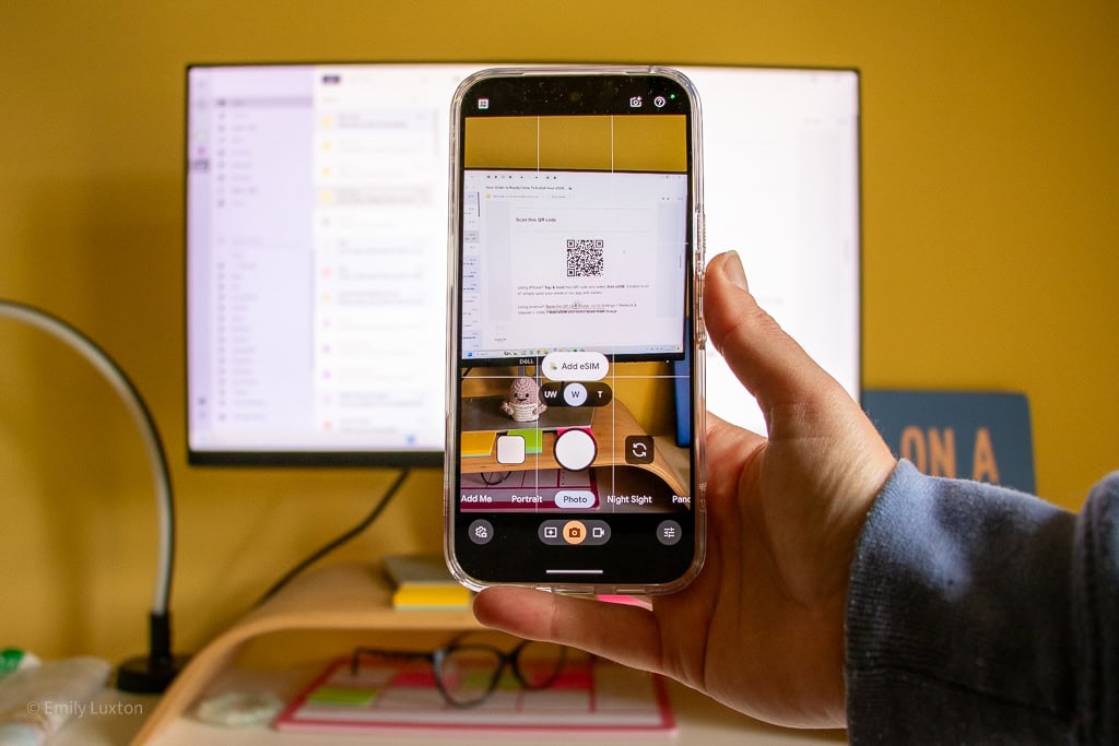 Hand holding a phone in front of a computor screen to scan a QR code
